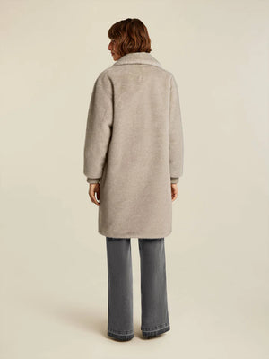 Person wearing a beige coat and blue jeans on a plain background