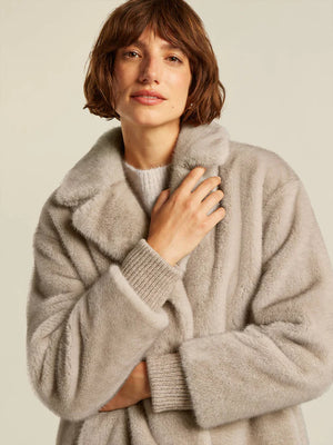 Woman wearing a light gray fluffy coat against a neutral background